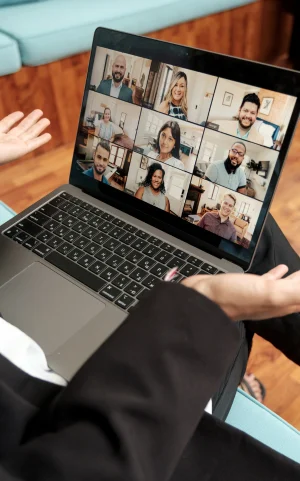 laptop displaying online meeting rests on someone's lap, person gestures with palms facing up